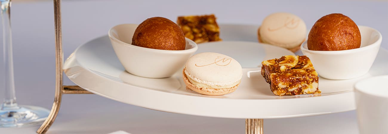 Assorted pastries and desserts displayed on white tiered serving plates, including macarons, chocolate truffles, and nutty co